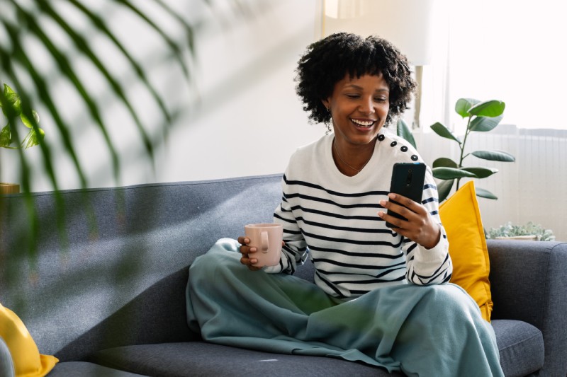 Young woman smiling at her smartphone while holding a mug