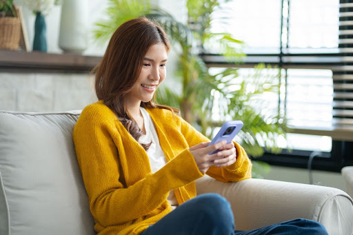 Woman wearing yellow cardigan sitting on her couch and smiling at smartphone