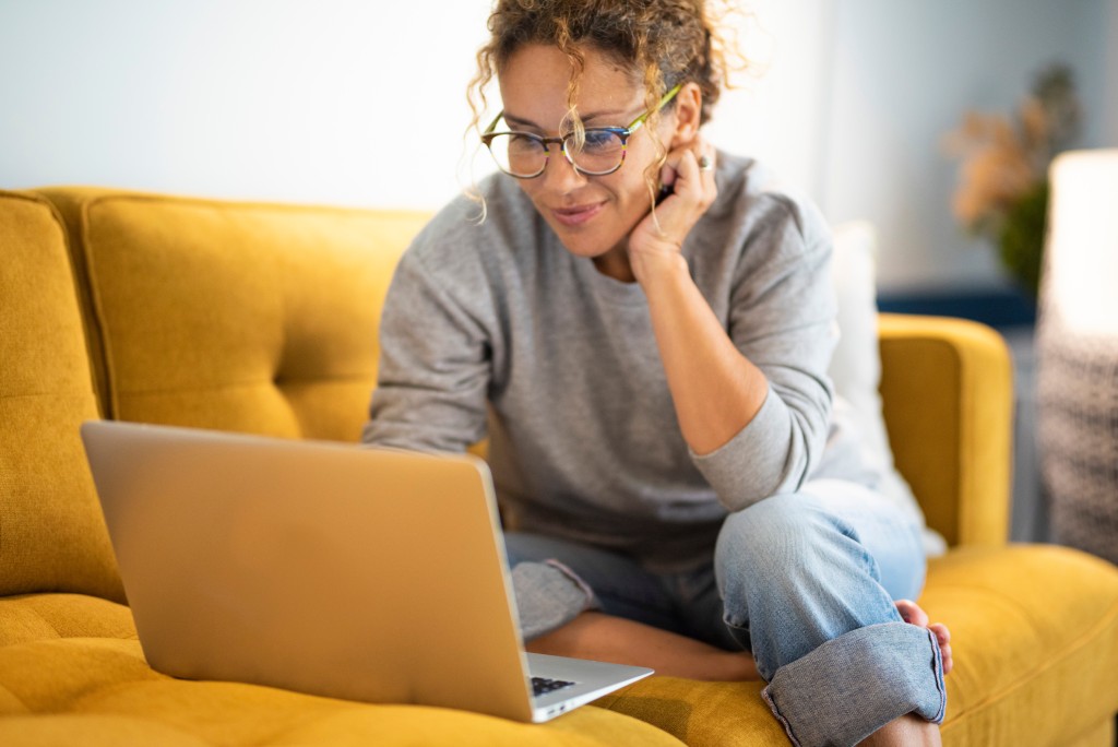 Woman sitting on a yellow couch using her laptop