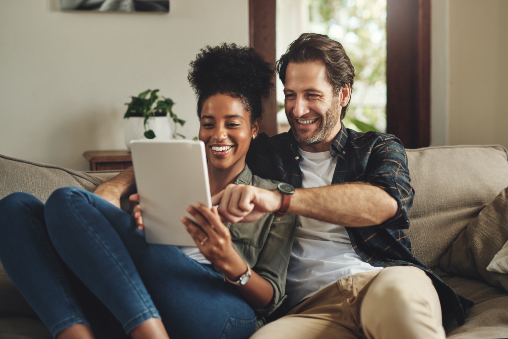Young couple using a digital tablet together while relaxing on a couch at home