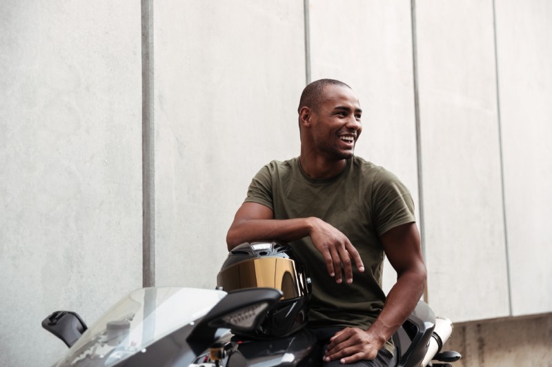 A man smiles on his parked motorcycle.