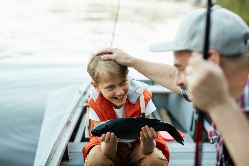 A boy proudly holds a fish he has caught from a boat